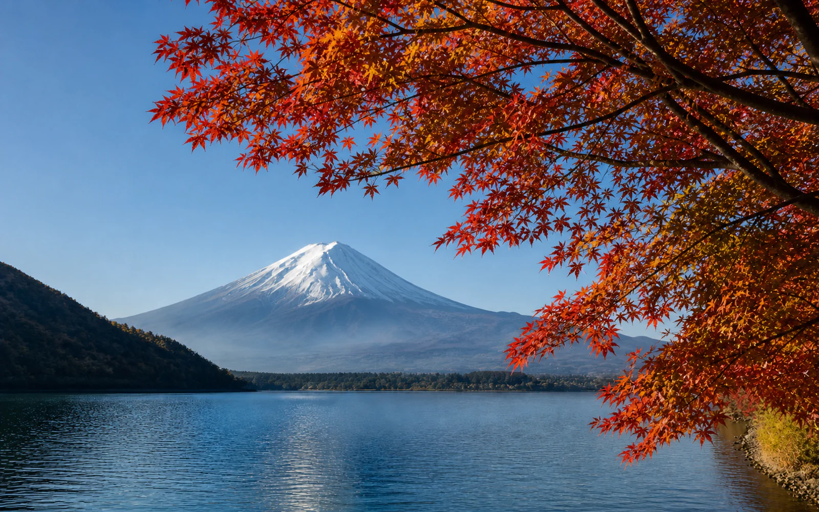 Snow-capped Mount Fuji framed by vivid red and orange maple leaves across Lake Kawaguchiko.