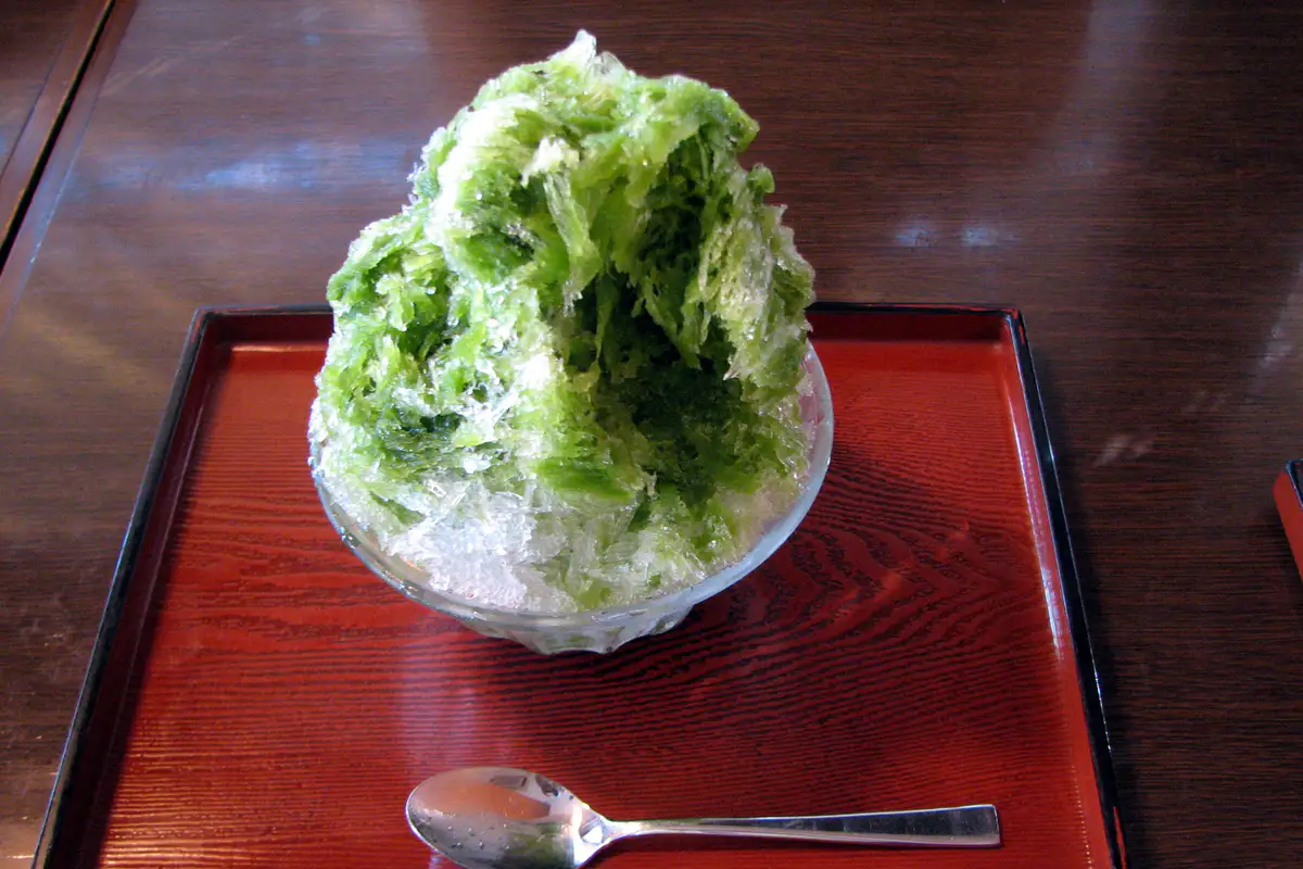 A tall bowl of matcha kakigori streaked with green tea syrup.