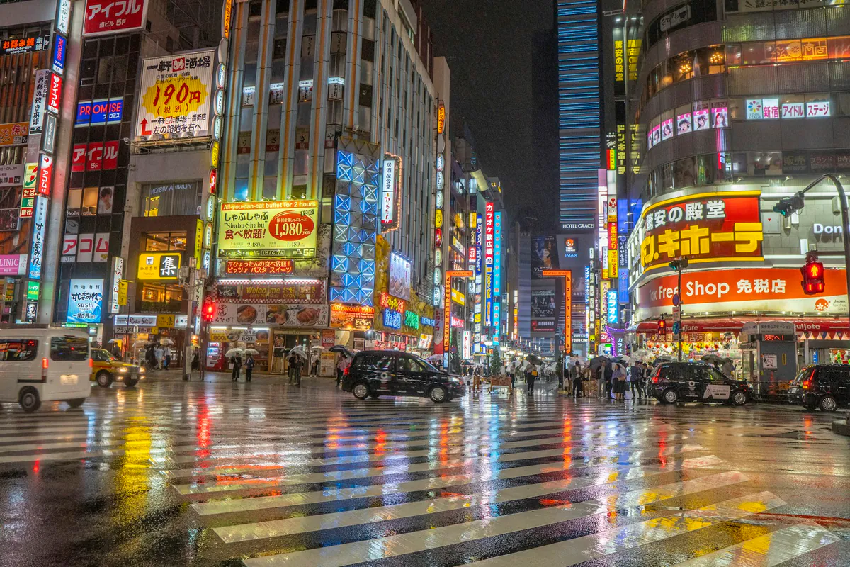 Pedestrians crossing a neon-lit Tokyo street on a rainy evening.