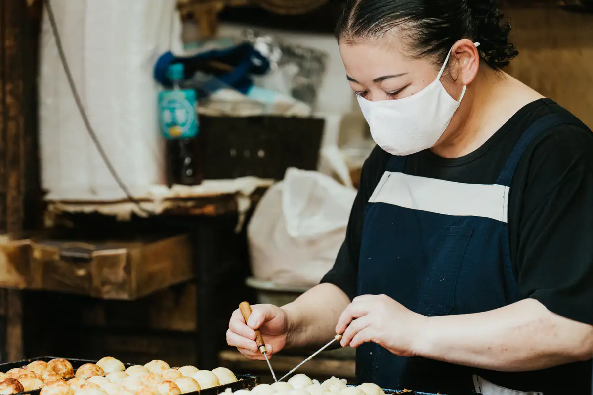 A vendor preparing Osaka street food on a hot griddle.