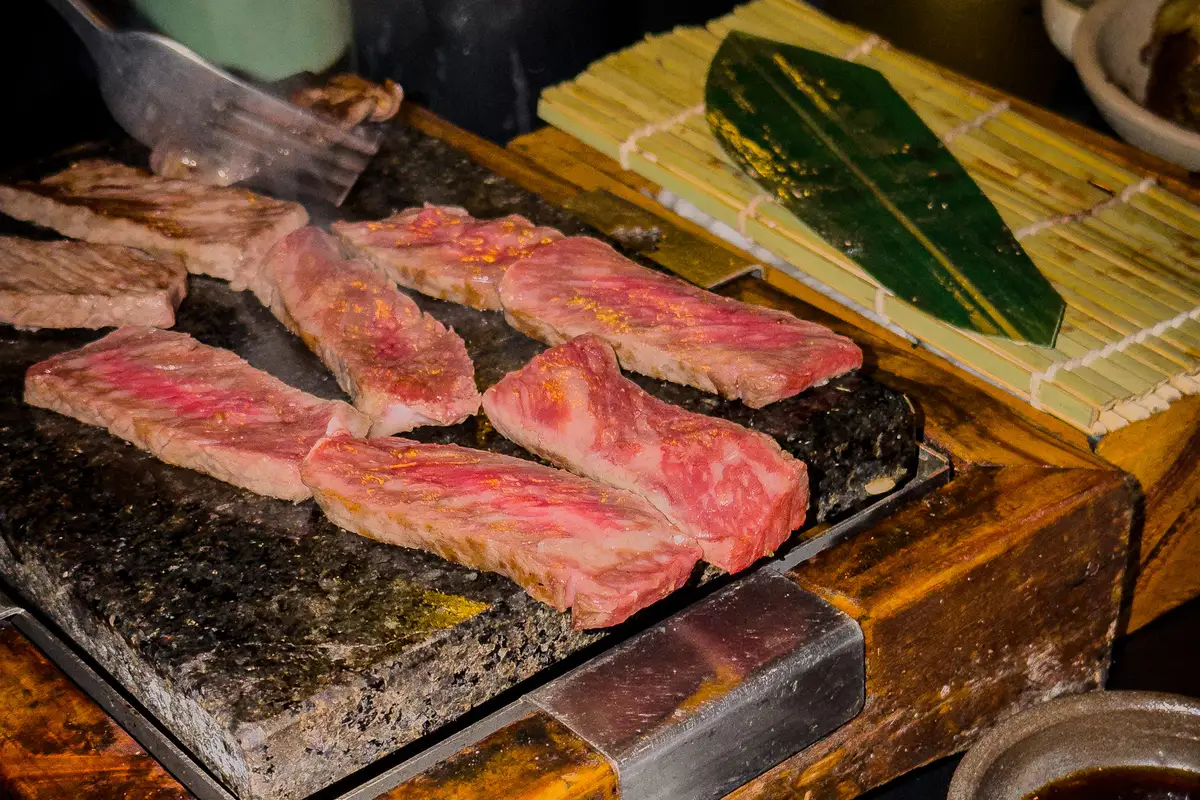 Marbled wagyu slices cooking on a tabletop hot-stone grill.